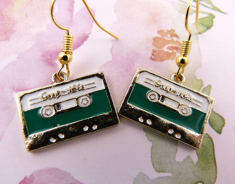 May include: Gold cassette tape earrings with a green background and white text that reads "Good Vibes".