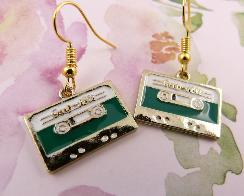 May include: Gold cassette tape earrings with a white background and green cassette tape. The earrings say "Good Vibes" on the cassette tape.