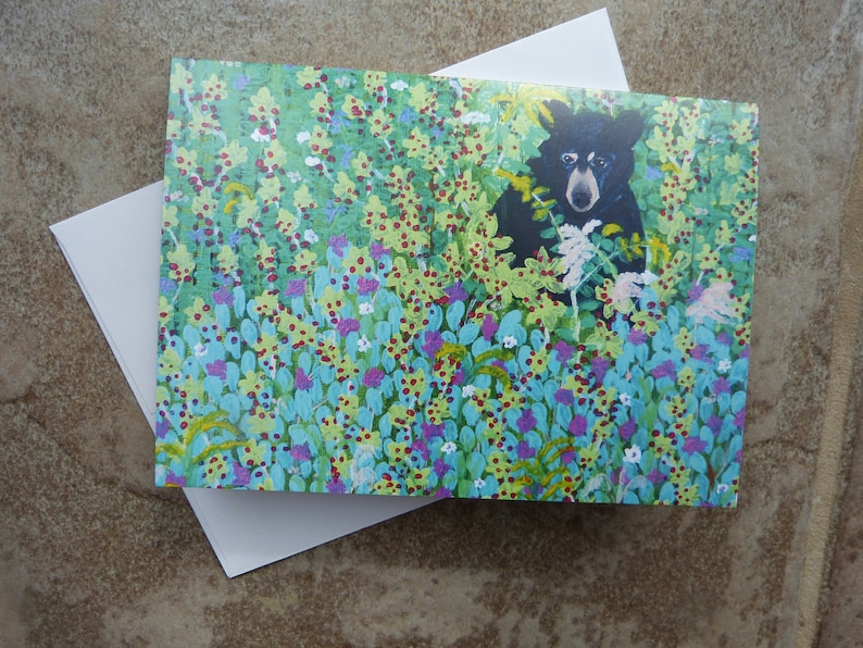 Pu&ograve; includere: Un orso nero che spunta da dietro un campo di fiori colorati. I fiori sono dipinti in tonalit&agrave; di blu, verde, giallo, viola e rosso.