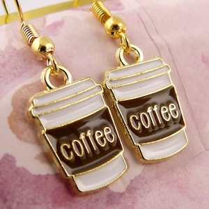 May include: Gold tone earrings with a coffee cup charm. The cup is white with a brown band and the word "coffee" written in gold letters.