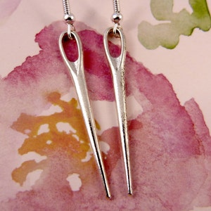 May include: A pair of silver needle earrings. The needles are long and thin, with a small loop at the top for the earring hook.