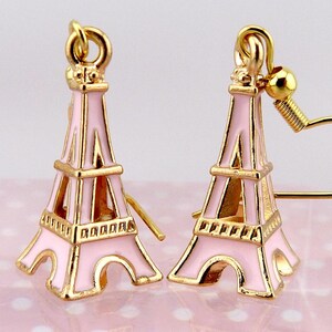 Peut inclure: Une paire de boucles d'oreilles représentant la Tour Eiffel, de couleur rose et dorée. Les boucles d'oreilles sont des répliques détaillées du célèbre monument parisien, avec une structure en métal doré et un remplissage en émail rose.