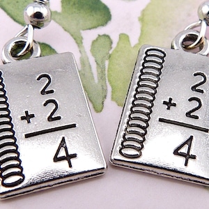 May include: Silver earrings shaped like a notebook with the math problem 2 + 2 = 4 written on the front.