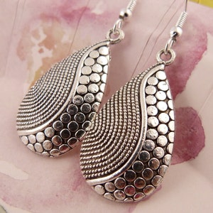 May include: A pair of silver teardrop earrings with a textured design. The earrings have a hammered finish and a dangling design.