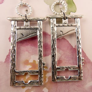 May include: A pair of silver guillotine earrings. The earrings are detailed with wood grain and a blade.