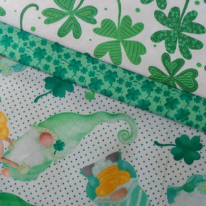 May include: Green fabric with a white background and a pattern of shamrocks. The fabric is folded over itself, showing a second layer of green fabric with a smaller shamrock pattern.