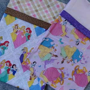 Pu&ograve; includere: Due pannelli di tessuto rosa e bianco con un motivo ripetuto di principesse Disney. Le principesse indossano abiti diversi e hanno colori di capelli diversi. Il tessuto &egrave; decorato con farfalle, corone e castelli.