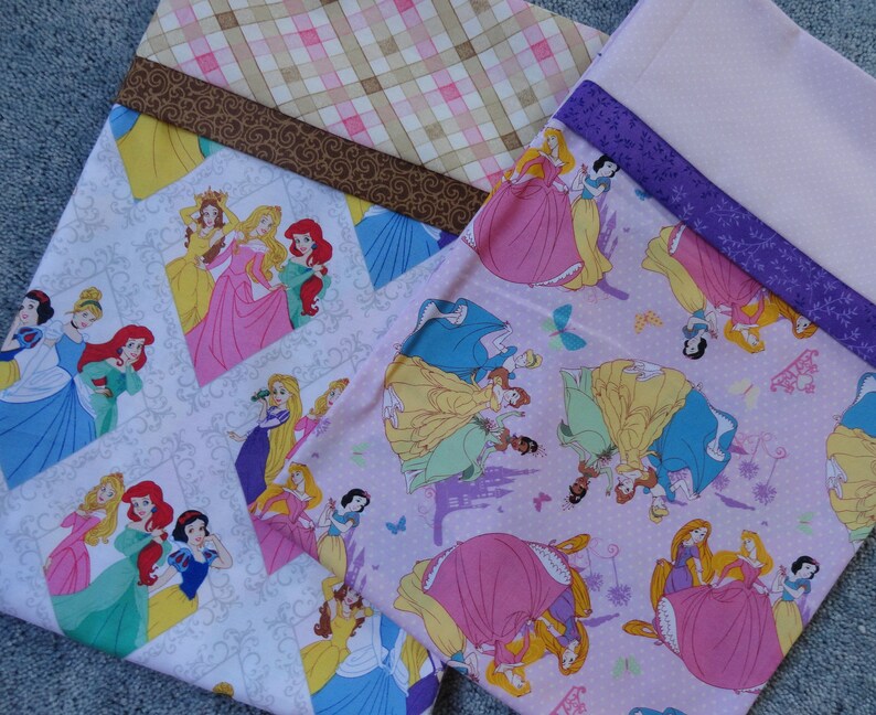 Pu&ograve; includere: Due pannelli di tessuto rosa e bianco con un motivo ripetuto di principesse Disney. Le principesse indossano abiti diversi e hanno colori di capelli diversi. Il tessuto &egrave; decorato con farfalle, corone e castelli.