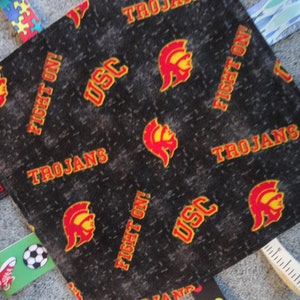 May include: A black and red fabric square with the words "Fight On!" and "USC Trojans" repeated. The fabric also features a red and yellow Trojan helmet logo.