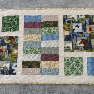 May include: A beige table runner with a patchwork design featuring various fabrics with horse, floral, and geometric patterns in shades of green, blue, brown, and beige.