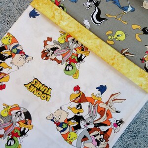 May include: White fabric with a repeating pattern of Looney Tunes characters, including Bugs Bunny, Daffy Duck, Tweety Bird, and Sylvester the Cat. The fabric has the words "Looney Tunes" printed on it.