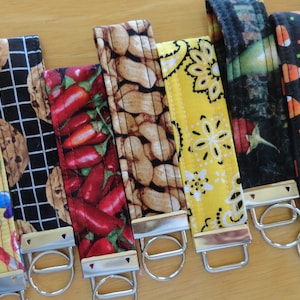 May include: A collection of ten colorful fabric keychains with different patterns, including peanuts, candy, chili peppers, and paisley. Each keychain has a silver metal ring.