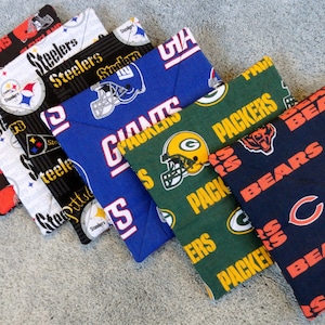 May include: Five fabric coasters featuring different NFL team logos. The coasters are in the colors of the teams: Browns, Steelers, Giants, Packers, and Bears.