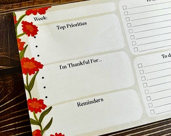 Op de afbeelding: Een weekplanner met een bloemige rand. De planner heeft secties voor "Week:", "Top Prioriteiten", "Ik ben dankbaar voor..." en "Herinneringen". Er zijn ook secties voor "Te doen voor werk" en "Te doen".