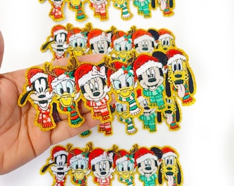 May include: Embroidered patches featuring Disney characters in Christmas attire. Mickey Mouse, Minnie Mouse, Donald Duck, and Pluto are depicted wearing Santa hats and scarves. The patches have gold trim and are on a white background.