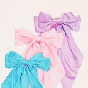 May include: Three satin ribbon bows in different colors: light blue, pink, and lavender. The bows are tied in a classic style with long tails.