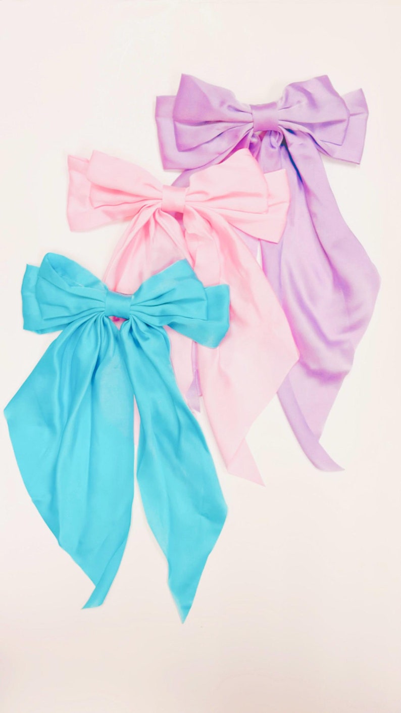 May include: Three satin ribbon bows in different colors: light blue, pink, and lavender. The bows are tied in a classic style with long tails.