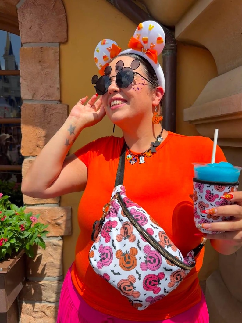 May include: A white headband with candy corn ears and an orange bow, black round sunglasses with mouse ear accents, a beaded necklace with character charms, and a white fanny pack featuring a pink and orange pumpkin mouse pattern with black bats.