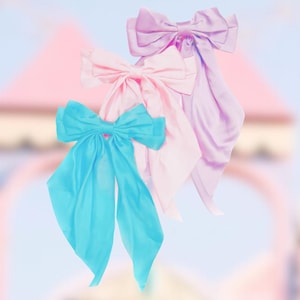 May include: Three satin ribbon bows in different colors: light blue, pink, and lavender. The bows are tied together and have long tails.