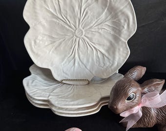 May include: A set of three white ceramic cabbage leaf-shaped serving plates. The plates are stacked on top of each other. The plates are decorated with a raised design that resembles a cabbage leaf.