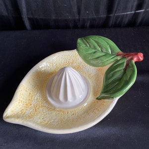 May include: A white ceramic lemon juicer with a green leaf design. The juicer has a white, ridged reamer in the center.
