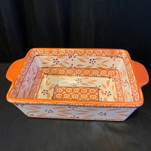 Op de afbeelding: Rechthoekige keramische ovenschaal met oranje handgrepen en rand. De binnenkant heeft een witte achtergrond met een herhalend bloemen- en bladerpatroon in tinten oranje en bruin. De schaal is ontworpen om te bakken en te serveren.