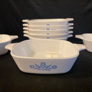 May include: A set of six white ceramic baking dishes with blue floral designs. The dishes are stacked on top of each other.