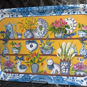 May include: Rectangular serving tray with a blue and white floral border. The tray's interior features a yellow background with shelves displaying vases, flowers, and decorative objects. A teapot, cat, and duck are also depicted.