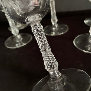 May include: Clear glass wine glasses with etched floral designs. The stems have a diamond-cut pattern. The glasses are on a dark surface. The image shows a close-up of the glasses.