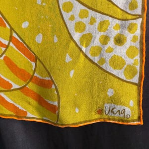 May include: A vintage silk scarf with a vibrant abstract design. The scarf features yellow, orange, and white patterns with an orange border. The scarf has the signature "Vera" in the corner.