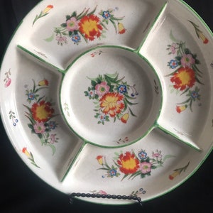 May include: A vintage divided serving platter with a white base and a green rim. The platter features floral designs with orange, pink, and blue flowers. The platter is divided into five sections.