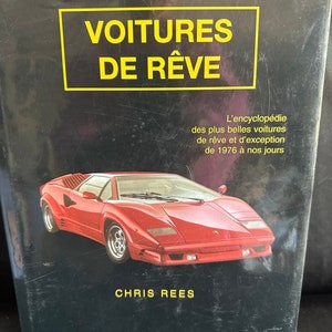May include: A book cover with the title "Voitures de Rêve" in yellow text on a black background. The book features a red sports car and the text "L'encyclopédie des plus belles voitures de rêve et d'exception de 1976 à nos jours" in white text. The author's name, "Chris Rees", is printed in yellow text at the bottom of the cover.