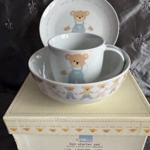 May include: A 3-piece starter set for children, featuring a white plate, bowl, and mug. Each piece is decorated with a cartoon bear wearing blue overalls. The set comes in a cream-colored box with the text "VIVA KIDS".