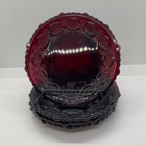 May include: A stack of ruby red glass plates. Each plate features a scalloped edge and a detailed embossed pattern of fruit and vines. The plates are arranged in a neat stack, showcasing their rich color and intricate design.
