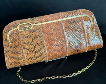 Könnte beinhalten: Eine braune Clutch aus Schlangenleder mit einer goldenen Kettenkette und einem einzigartigen goldenen Verschluss.