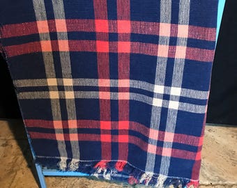 Op de afbeelding: Een blauw geruite deken met rode, witte en roze accenten is over een lichtblauw metalen rek gedrapeerd. De deken heeft een gefranjerde rand. Het ruitpatroon is een klassiek ontwerp.