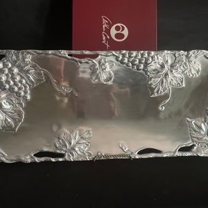 May include: A silver serving tray with a grapevine design. The tray is rectangular and has a raised edge. The grapevine design is embossed and includes leaves and grapes.
