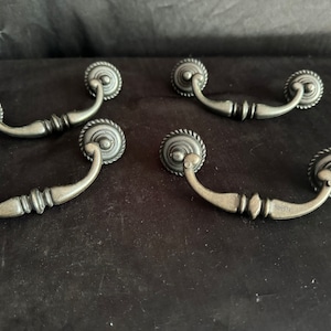 May include: Four antique-style drawer pulls with a silver finish. Each pull features a circular backplate with a rope-like border and a curved handle. The hardware is designed for furniture restoration or new builds.