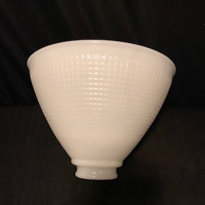 May include: White glass lampshade with a textured, grid-like pattern. The lampshade has a flared, conical shape and a small base. The lampshade is made of opaque glass.
