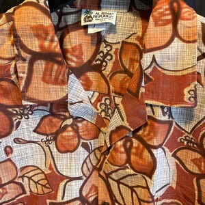May include: A button-down shirt with a large floral pattern in shades of brown, tan, and cream. The shirt has a collared neckline and short sleeves. The tag reads "ALOHA REPUBLIC MADE IN HAWAII".