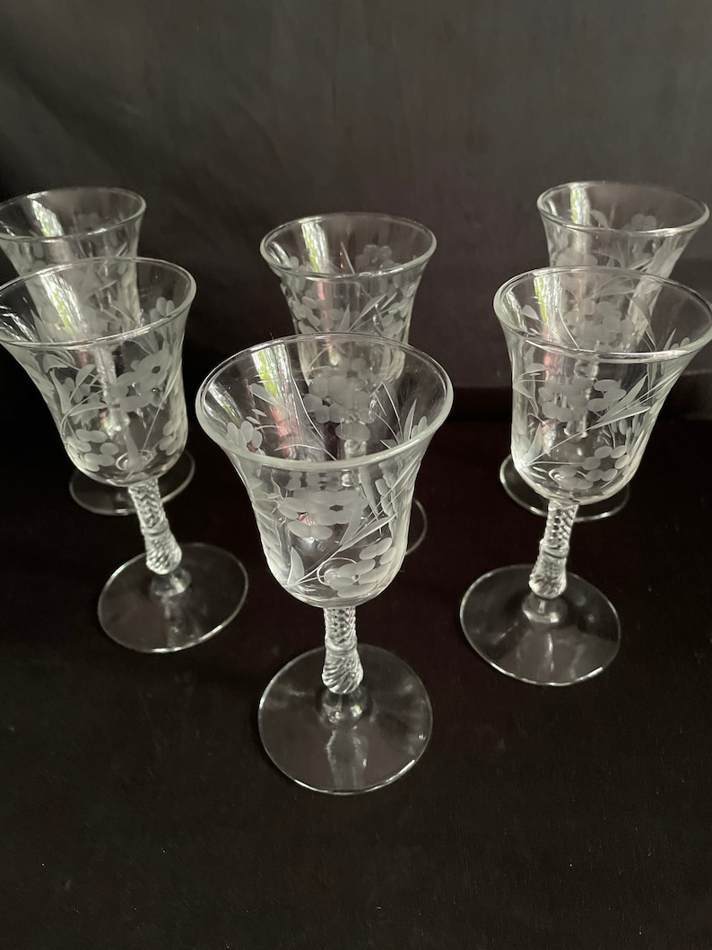 May include: Six clear glass cordial glasses with etched floral designs. Each glass features a flared bowl, a twisted stem, and a round base. The etched floral pattern is visible on the bowl of each glass.