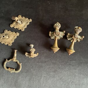May include: An assortment of antique brass hardware pieces, including ornate drawer pulls and decorative backplates. The hardware has a vintage aesthetic, with detailed designs and a tarnished finish. The collection includes various shapes and sizes, suitable for furniture restoration.