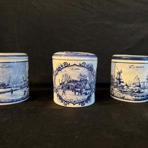 May include: Three blue and white ceramic canisters with Dutch scenes depicting the four seasons. The canisters are labeled "Winter", "Lente" (Spring), and "Zomer" (Summer).