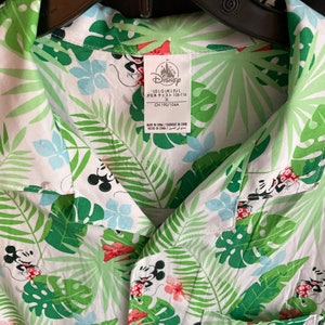 May include: White button-up shirt with a tropical leaf and Mickey Mouse print. The shirt features green, blue, and red accents. The Disney logo is visible on the tag.