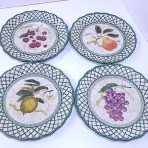May include: A set of four round ceramic plates with a scalloped, green lattice-patterned rim. Each plate features a central off-white surface with a crackle glaze finish and a different hand-painted fruit illustration: raspberries, a pear, a lemon, and grapes.