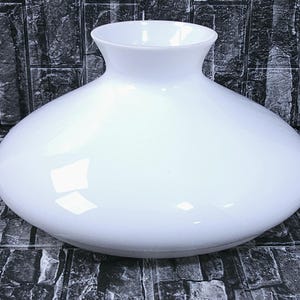 May include: A smooth, white, opaque glass lamp shade with a wide, rounded, bulbous body and a flared, open top. The surface of the glass is glossy and reflective, showing light highlights on its curved exterior. The shade has a simple, clean design.
