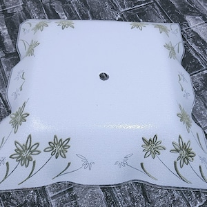 May include: A square, frosted glass light fixture cover with a floral design. The white cover has a scalloped edge and is decorated with gold and green flowers and leaves. A single hole is in the center.