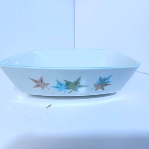 May include: A white rectangular baking dish with a light blue rim and a design of three brown and blue leaves.