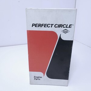 May include: A rectangular white cardboard box for Perfect Circle engine parts. The front features a large red graphic shape on the left and a black graphic shape on the right. The text reads Perfect Circle with a Dana logo and Engine Parts.
