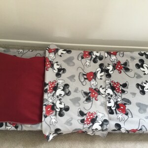 May include: A gray pet bed with a red pillow. The bed has a pattern of Mickey and Minnie Mouse in black, white, and red. Gray hearts are also on the bed.